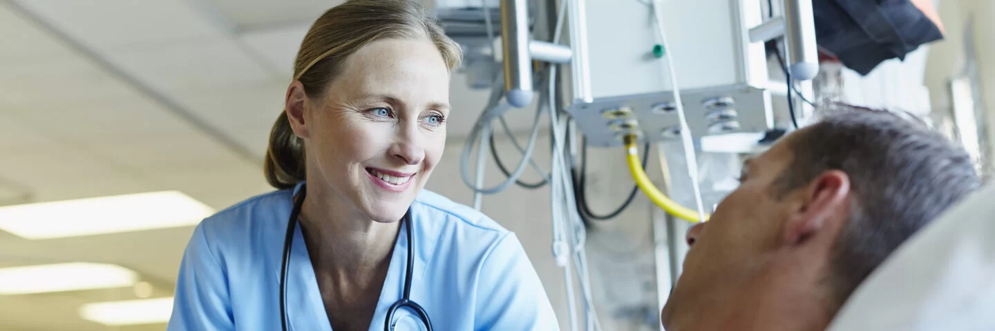 Smiling doctor looking at patient in hospital ward.