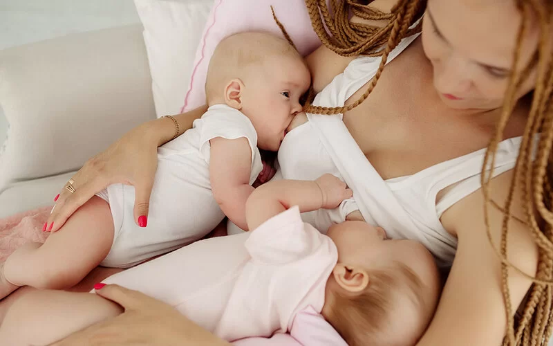 Eine Frau, die gerade eine Mehrlingsgeburt hinter sich hat, stillt ihre neugeboren Zwillinge.