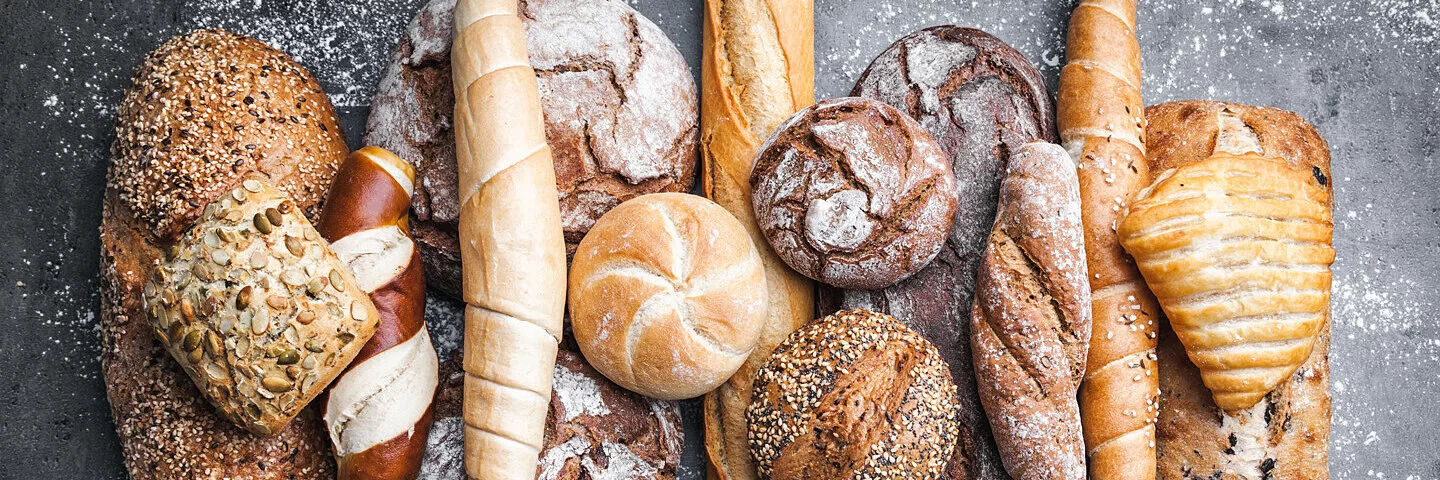 Auf einem Tisch liegen unterschiedliche Brotlaibe, Brötchen und andere Backwaren.