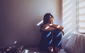 Frau mit Depressionen sitzt auf ihrem Bett vor dem Fenster.