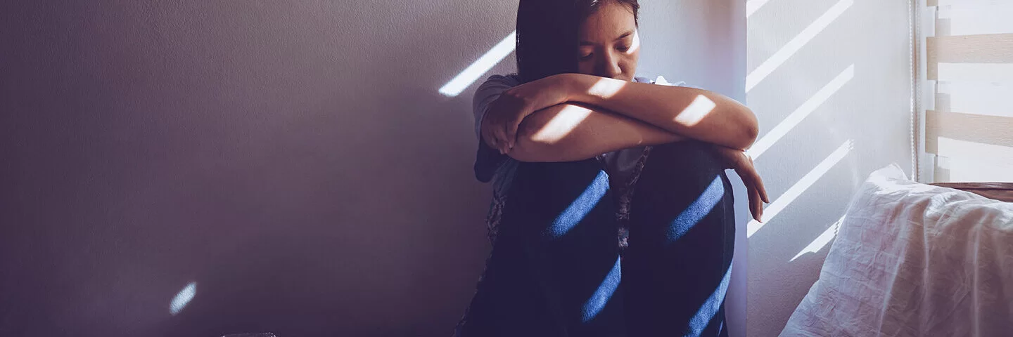 Frau mit Depressionen sitzt auf ihrem Bett vor dem Fenster.