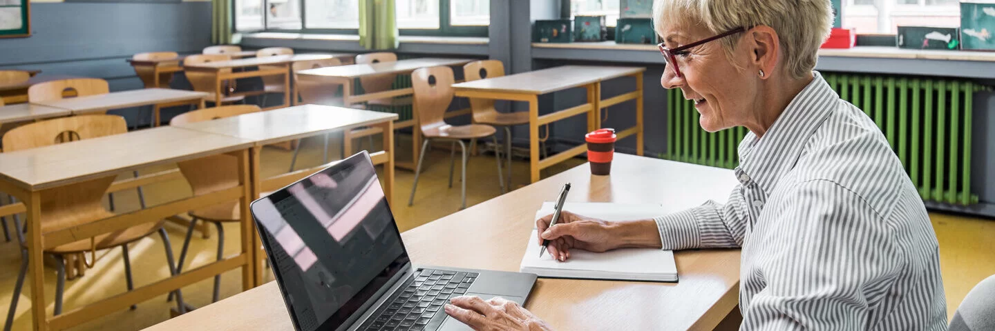 Eine Frau arbeitet mit ihrem Laptop im Klassenzimmer. Sie meldet sich für den Henrietta-Live-Webcast an.