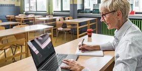 Eine Frau arbeitet mit ihrem Laptop im Klassenzimmer. Sie meldet sich für den Henrietta-Live-Webcast an.