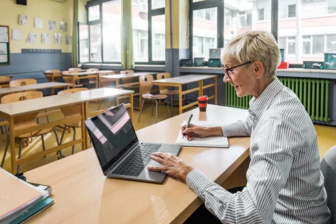 Eine Frau arbeitet mit ihrem Laptop im Klassenzimmer. Sie meldet sich für den Henrietta-Live-Webcast an.