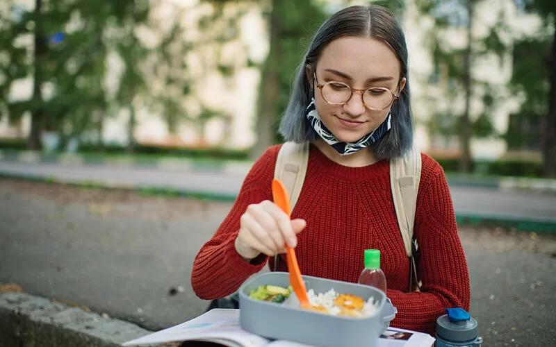 Studentin macht im Freien Pause und isst aus ihrer Bento-Box.