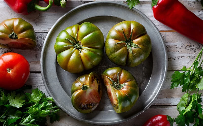 Auf einem Zinnteller liegen drei grüne Tomaten, eine davon aufgeschnitten.