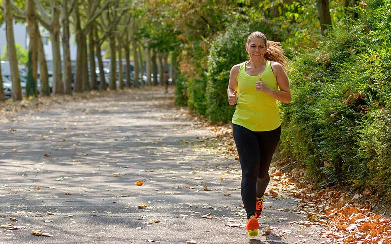 Eine Frau joggt einen von Bäumen gesäumten Fußweg entlang.