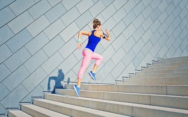Eine junge Frau in Sportkleidung läuft dynamisch eine Treppe hinauf.
