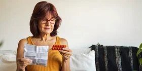 Eine Person hält orale Antibiotika in der Hand, die Packung liegt auf dem Tisch.