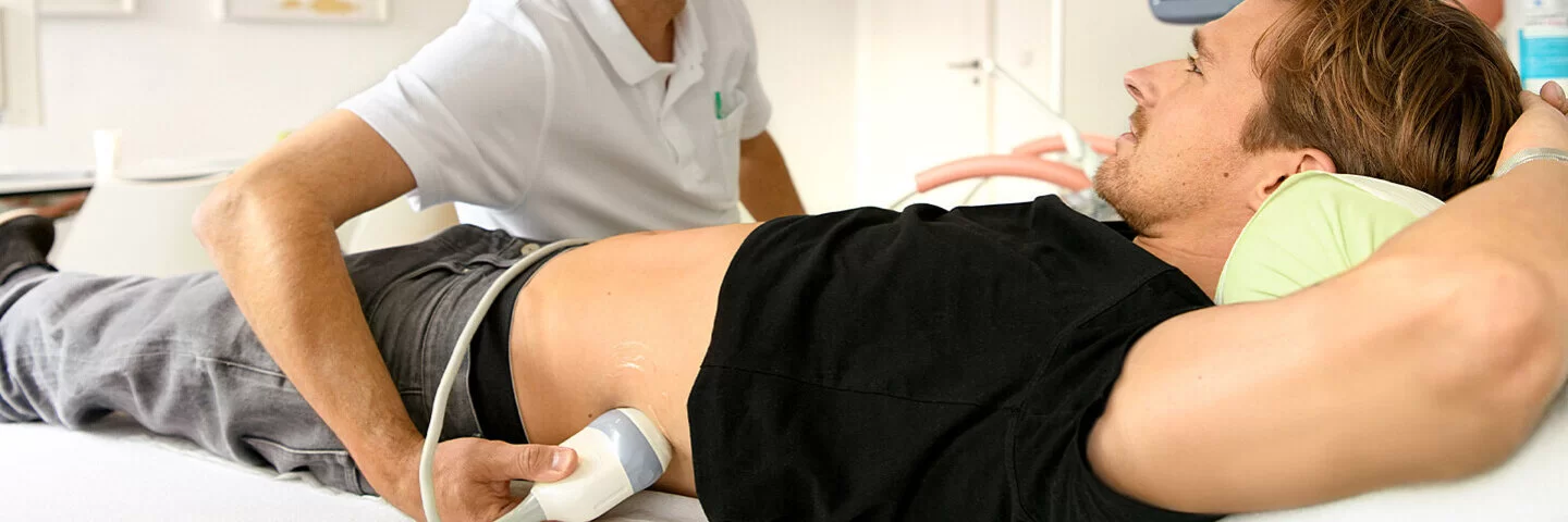 Ein Arzt untersucht mit einem Ultraschallgerät die Nieren eines jungen Mannes.