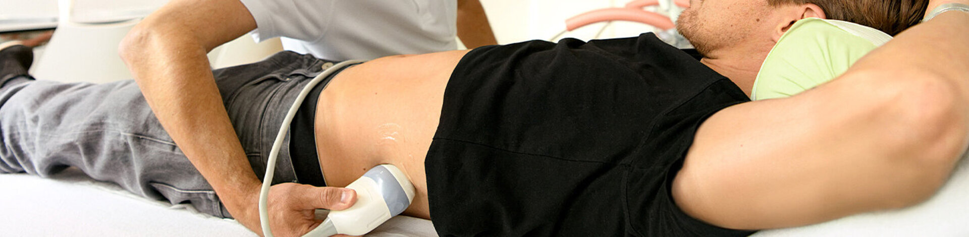 Ein Arzt untersucht mit einem Ultraschallgerät die Nieren eines jungen Mannes.