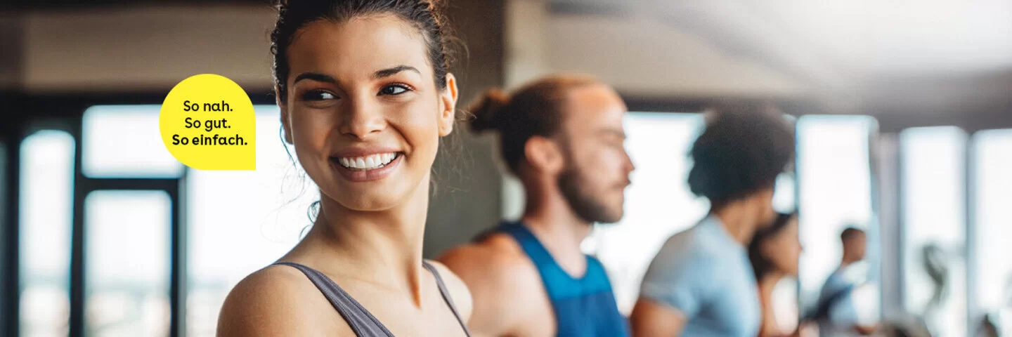 Eine junge Frau steht in einem Fitness-Studio auf einem Laufband und lacht in die Kamera