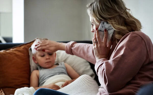 Mutter umsorgt ihr krankes Kind und ruft den Arzt für einen fachärztlichen Rat an.
