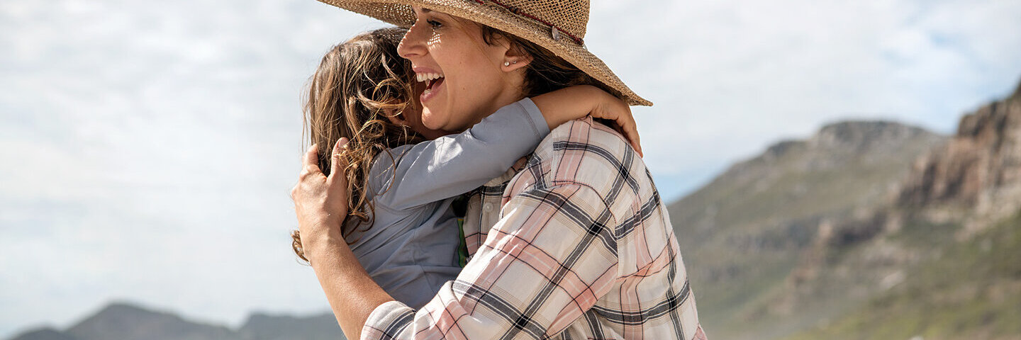 Eine Frau umarmt ihr Kind am Strand – sie erholen sich im Urlaub.