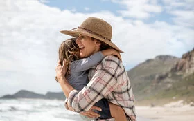 Eine Frau umarmt ihr Kind am Strand – sie erholen sich im Urlaub.