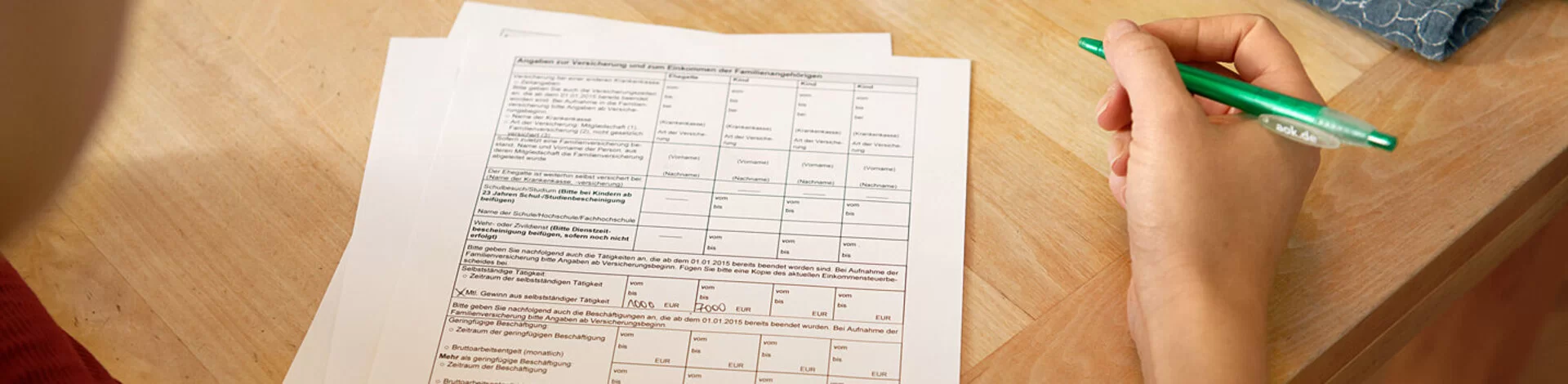 Eine Frau sitzt an einem Tisch mit mehreren Zetteln vor sich. In der Hand hält sie einen Stift. Die AOK stellt alle wichtigen Leistungsanträge und Formulare zusammen.