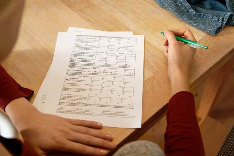 Eine Frau sitzt an einem Tisch mit mehreren Zetteln vor sich. In der Hand hält sie einen Stift. Die AOK stellt alle wichtigen Leistungsanträge und Formulare zusammen.