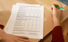 Eine Frau sitzt an einem Tisch mit mehreren Zetteln vor sich. In der Hand hält sie einen Stift. Die AOK stellt alle wichtigen Leistungsanträge und Formulare zusammen.