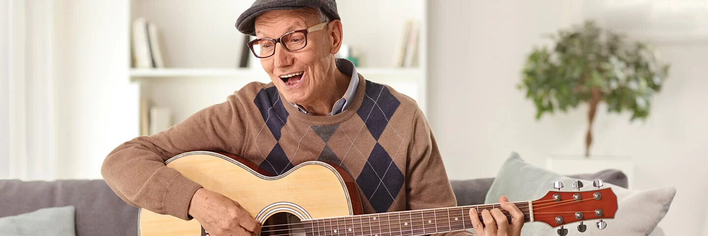 Mann sitzt auf dem Sofa vor einem Laptop und lernt Gitarre im Alter.