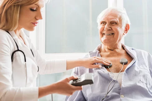 Kardiologin bereitet älteren Patienten für ein EKG vor.
