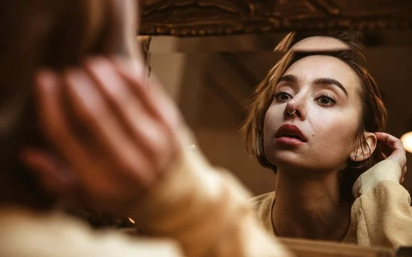 Eine Frau betrachtet ihr Nasen-Piercing im Spiegel.