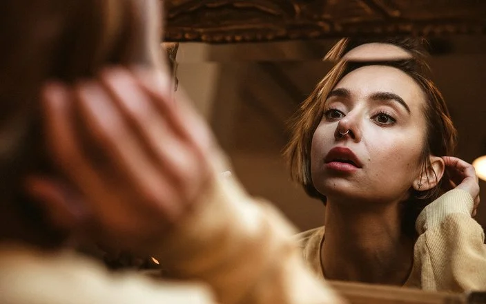 Eine Frau betrachtet ihr Nasen-Piercing im Spiegel.