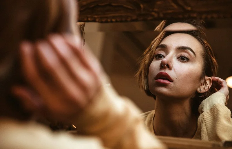 Eine Frau betrachtet ihr Nasen-Piercing im Spiegel.