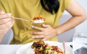 Eine Frau hat Magenschmerzen beim Essen und hält sich die Hand vor den Bauch.