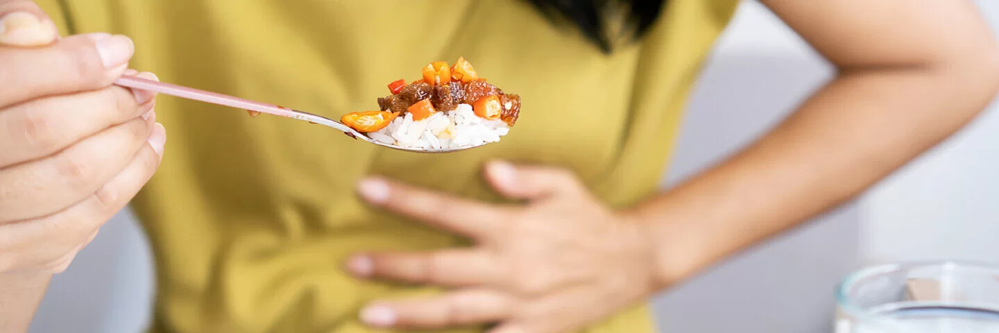 Eine Frau hat Magenschmerzen beim Essen und hält sich die Hand vor den Bauch.