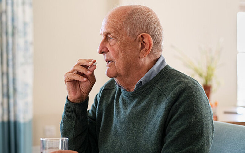 Ein älterer Mann nimmt eine Tablette gegen seine Schmerzen ein.