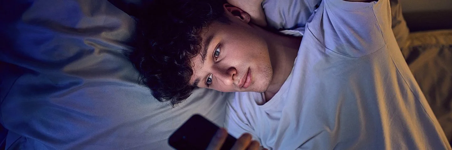 Ein Jugendlicher liegt im Bett und schaut auf sein Handy.