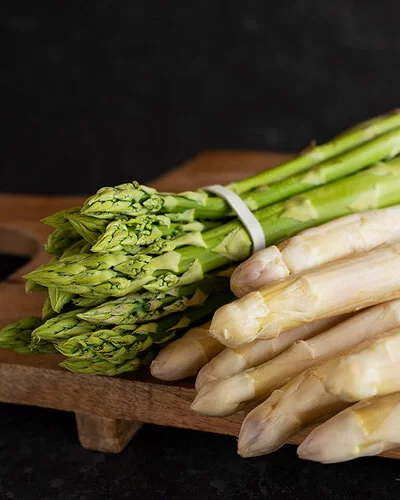 Grüner und weißer Spargel liegen auf einem Holzbrett.