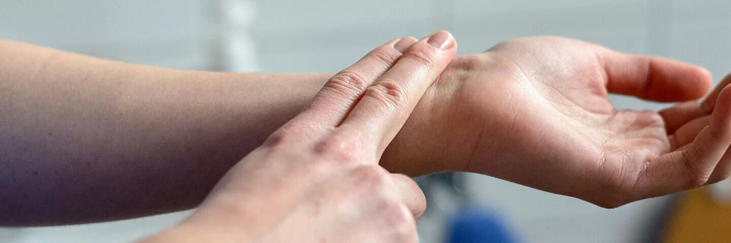 Eine Person legt zwei Finger auf die Unterseite ihres linken Handgelenks, um den Puls zu messen.