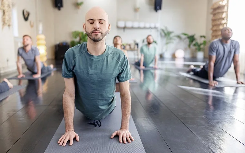 Gruppe von Erwachsenen macht in einem Kursraum Yoga-Übungen auf Matten.