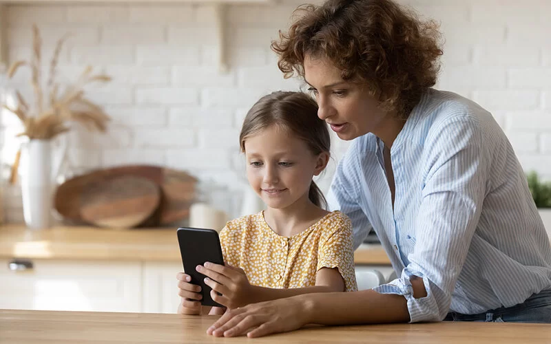 Eine Mutter erklärt ihrer kleinen Tochter die Nutzung des Smartphones.