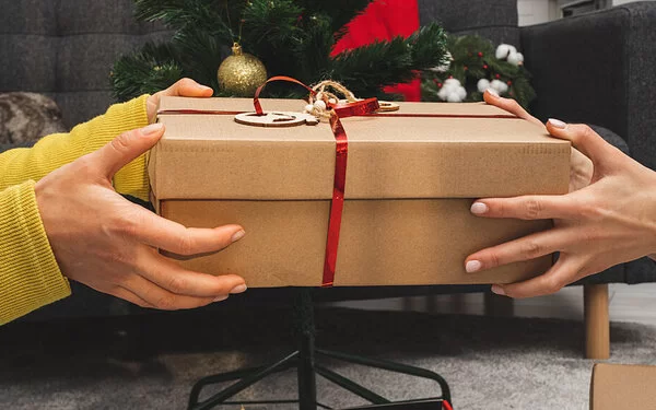 Eine Person überreicht ein Weihnachtsgeschenk in einem Schuhkarton.