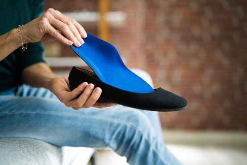 Eine Frau legt eine orthopädische Schuheinlage in einen Ballerina-Schuh. Die AOK übernimmt unter bestimmten Voraussetzungen die Kosten.