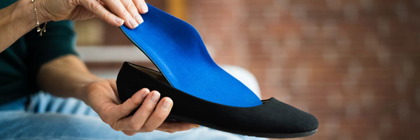 Eine Frau legt eine orthopädische Schuheinlage in einen Ballerina-Schuh. Die AOK übernimmt unter bestimmten Voraussetzungen die Kosten.