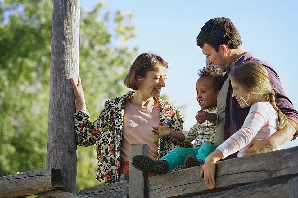 Eine Familie mit 2 kleinen Kinder steht an einem Holzzaun.