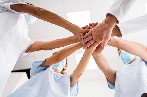 Vier Menschen in Krankenhauskleidung stehen im Kreis zusammen und legen die Hände übereinander. Das Ärzteteam der AOK-Zahnklinik lebt die Gemeinschaft.