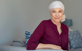 Eine an Brustkrebs-erkrankte Frau trägt ein Kopftuch und lächelt in die Kamera.
