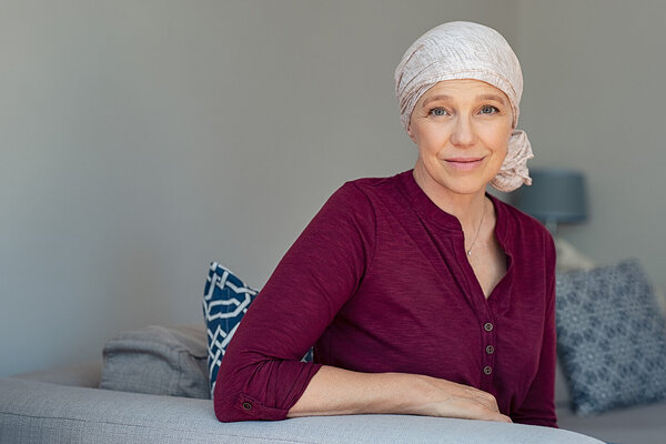 Eine an Brustkrebs-erkrankte Frau trägt ein Kopftuch und lächelt in die Kamera.