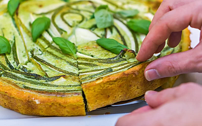 Jemand greift nach einem Stück Zucchini-Tarte.