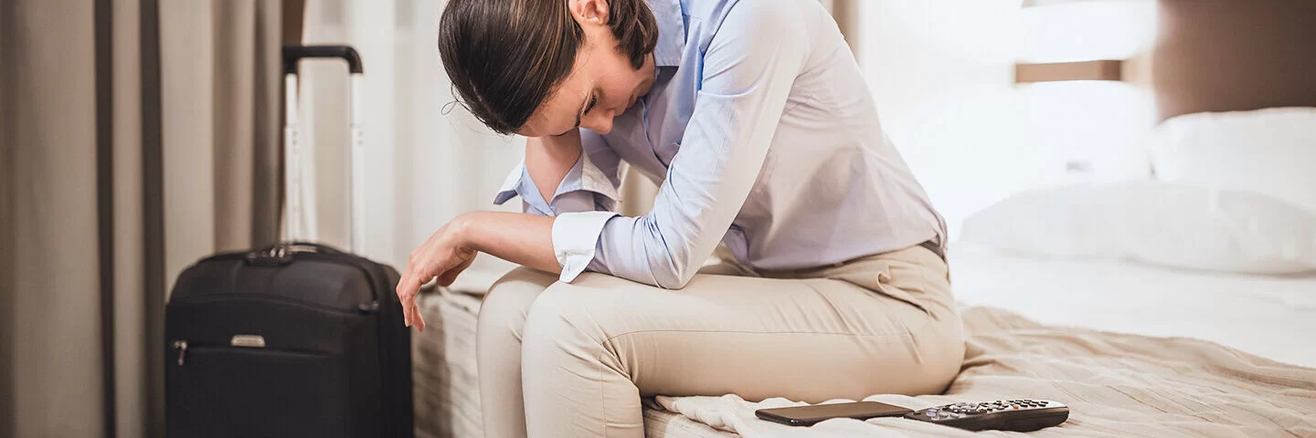 Eine Frau sitzt auf dem Bett ihres Hotelzimmers und ist nach der Flugreise erschöpft. Sie hat Jetlag.