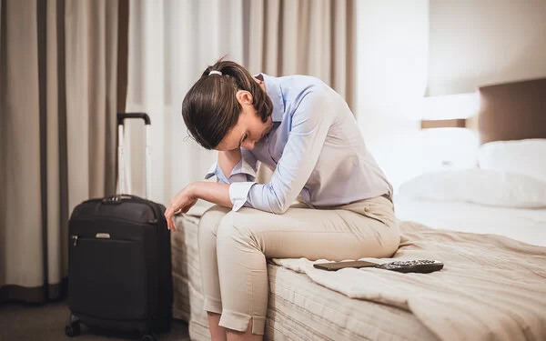 Eine Frau sitzt auf dem Bett ihres Hotelzimmers und ist nach der Flugreise erschöpft. Sie hat Jetlag.