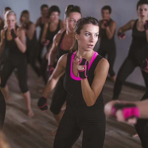 Im Fokus sind zwei Frauen in Box-Pose zu sehen, 17 weitere Frauen in der Unschärfe. Die gesamte Piloxing-Gruppe trägt fingerlose, schwarz-pinke Handschuhe und überwiegend schwarz-pinke Sportkleidung.