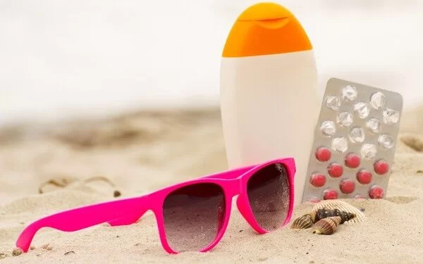 Sonnenbrille, Sonnenmilch und Arzneimittel liegen im Sandstrand