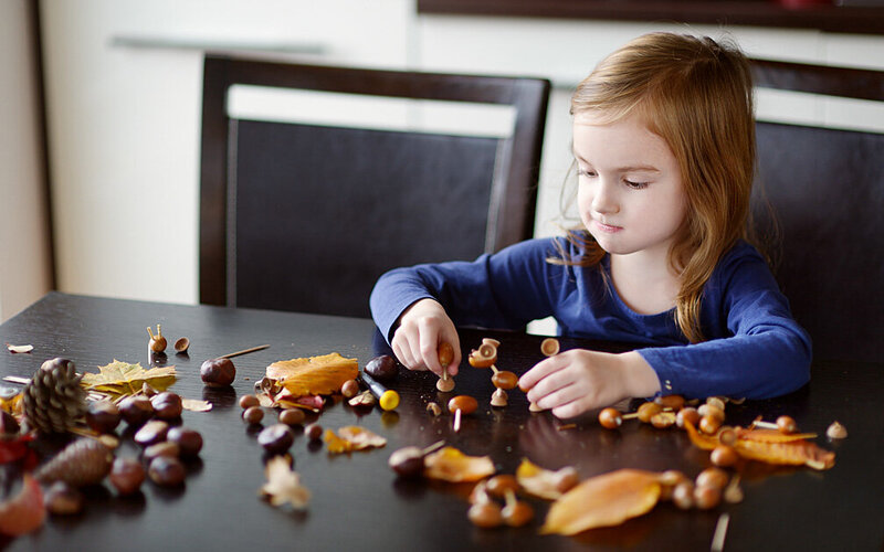 Ein Mädchen sitzt am Küchentisch und spielt mit Kastanien.