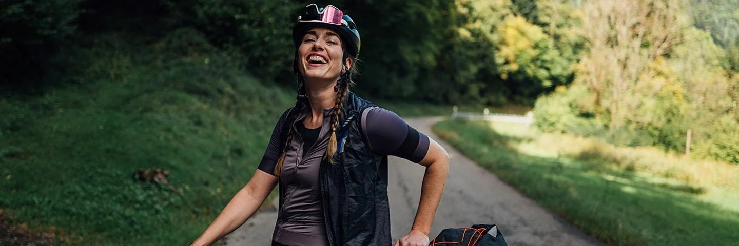 Lachende Frau steht mit dem Fahrrad auf einer Landstraße im Grünen.