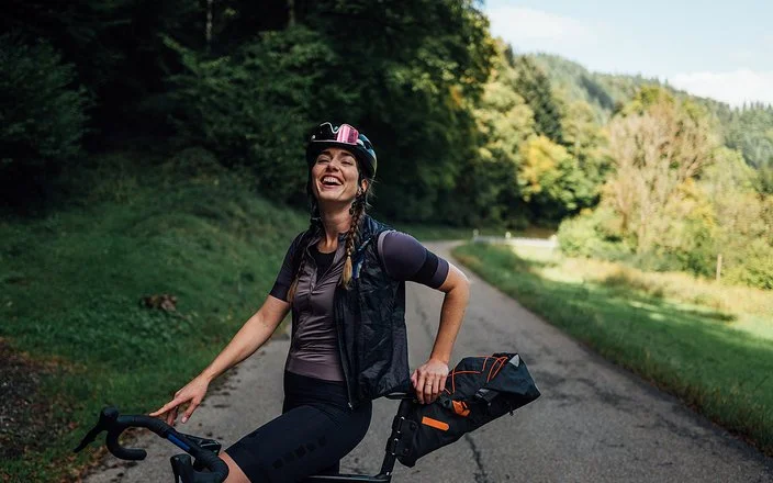 Lachende Frau steht mit dem Fahrrad auf einer Landstraße im Grünen.